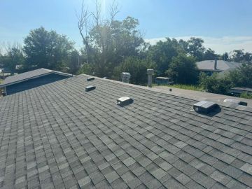 Residential shingle roof with vents and skylights under a clear sky