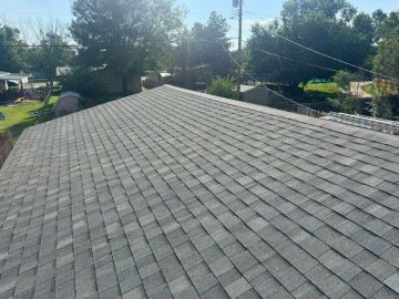 New asphalt shingle roof on a residential home with trees and power lines in the background